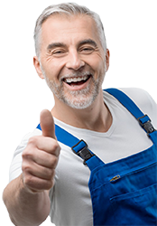 Lächelnder Mann mit kurzen grauen Haaren und Bart, der ein weißes Hemd und einen blauen Overall trägt und den Daumen nach oben zeigt.